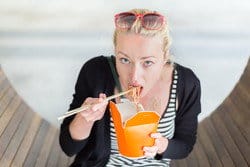 スペインで木のベンチに座って麺を食べる女性。