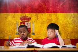 2 人の子供がスペインの国旗の前の机に座っています。