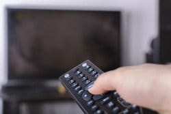 テレビの前でリモコンを持ちながらスペインの番組を見ている人がいます。