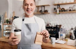 エプロンを着たスペイン人男性がコーヒーを持っている。