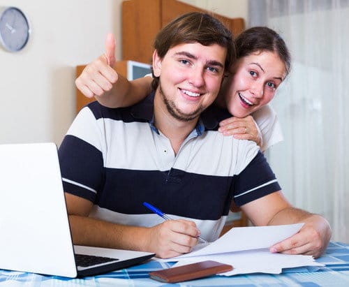 スペインでラップトップを持ちテーブルに座りながら親指を立てる若いカップル。