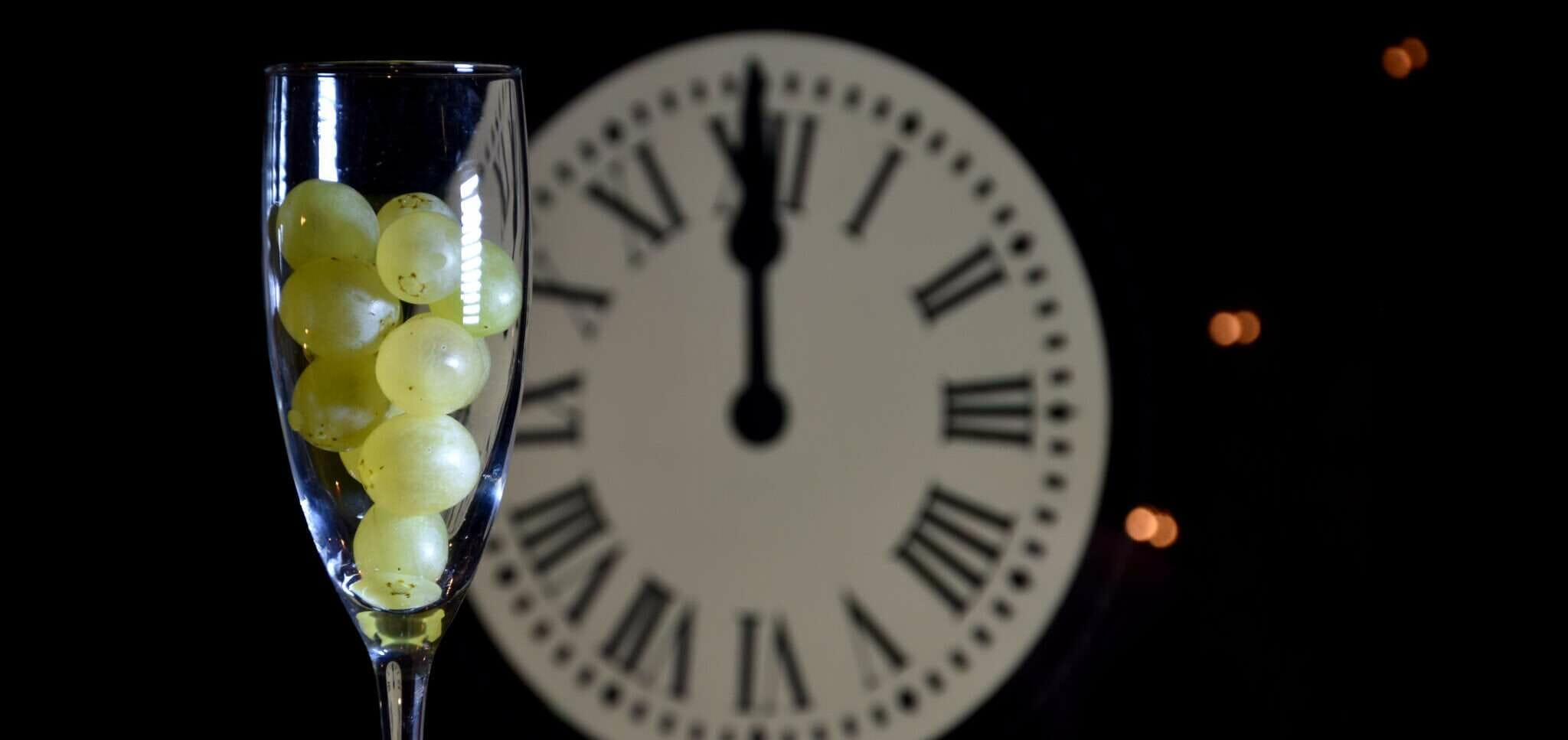 時計の前にブドウの入ったスペインのシャンパン グラス。
