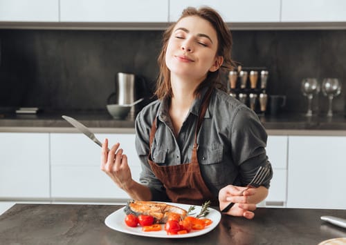 エプロンを着た女性がキッチンでスペインの味と技術を取り入れた料理を作っています。