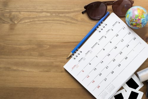 木製テーブルの上にカレンダー、サングラス、地球儀が置かれ、スペインが表示されています。