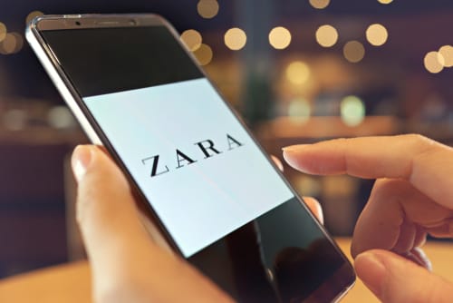 スペインの人気ブランド「ZARA」のロゴが入ったスマートフォンを持つ人物。