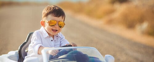 スペインの若い少年がサングラスをかけながらおもちゃの車を運転しています。