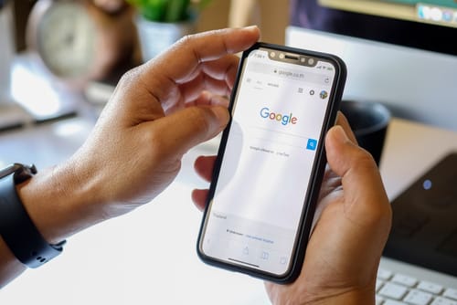 Google 検索が表示された携帯電話を持ち、スペインを検索している人。