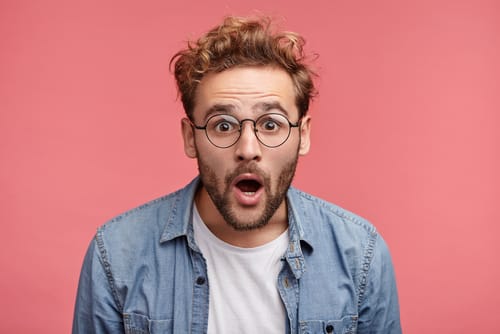 スペインのピンクの背景に眼鏡をかけた男性が驚いた表情をしている。