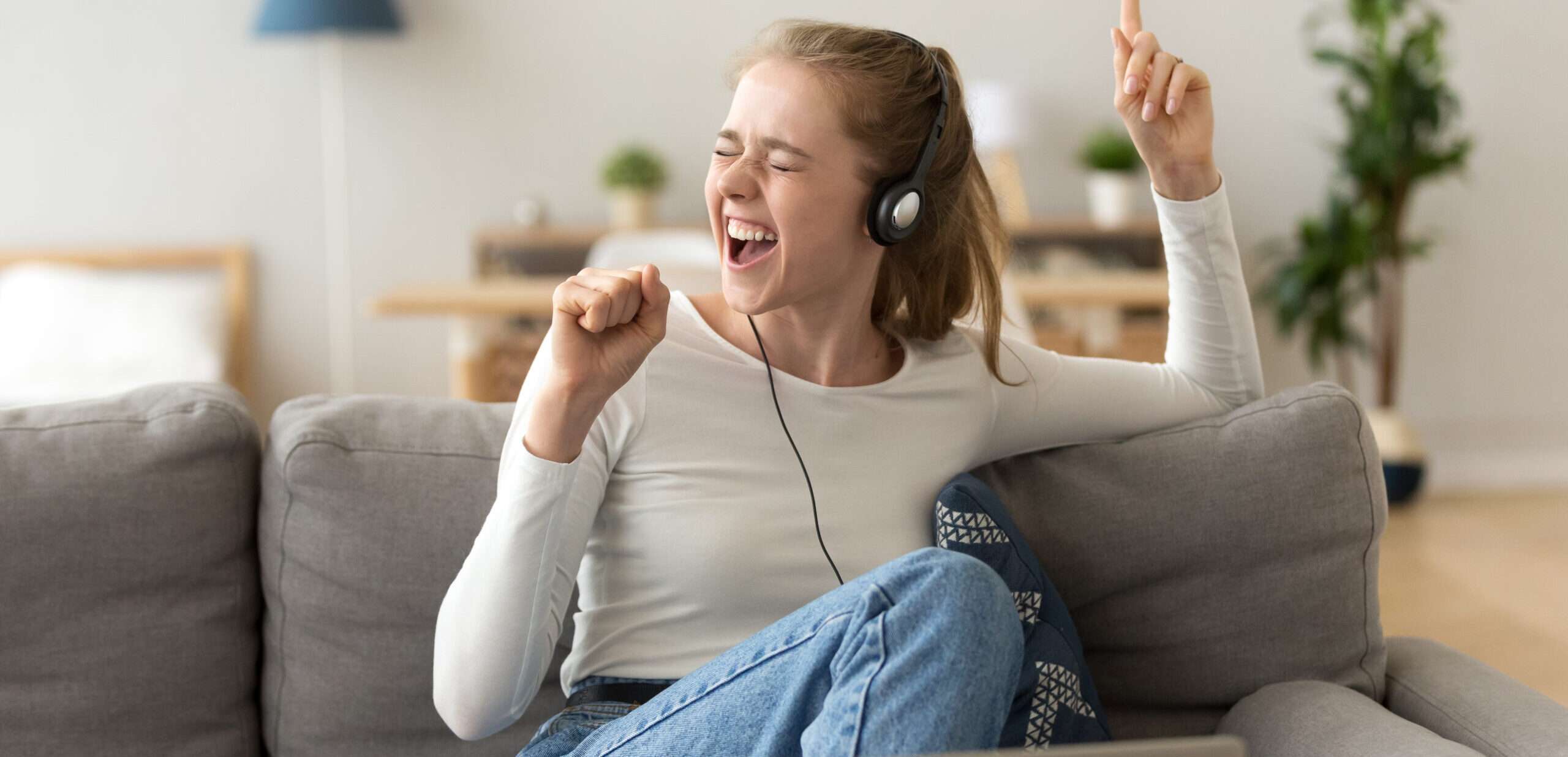 若い女性がソファに座りながらラップトップでスペイン語のヒット曲を聞いています。