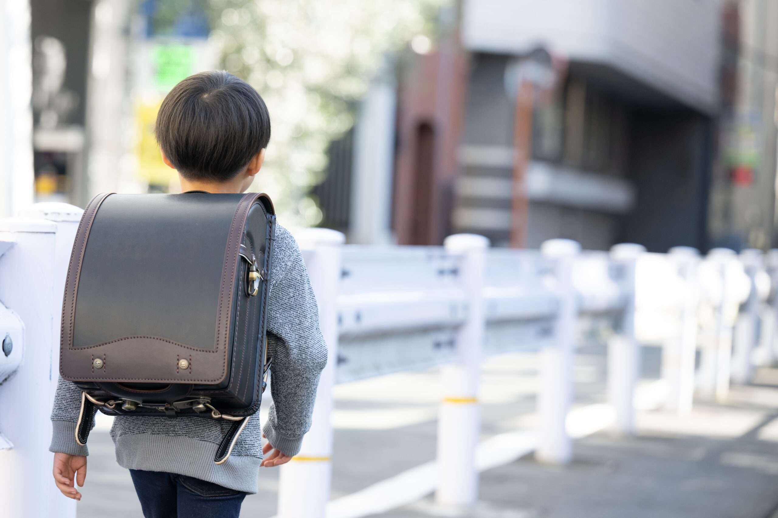 バックパックとランドセルを背負って道を歩く少年。