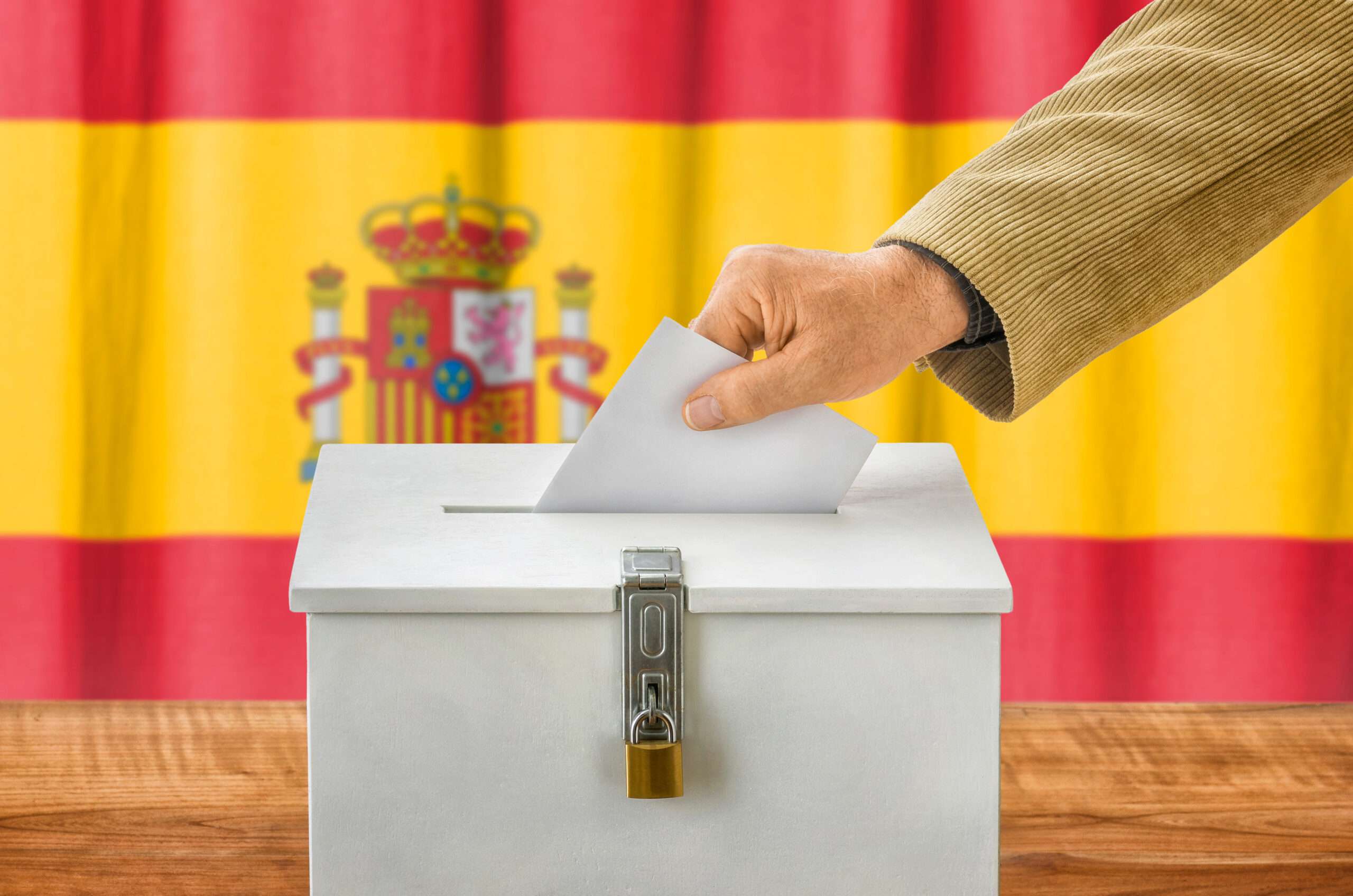 スペイン国旗の前の箱に置かれているスペイン語の政治と選挙に関する投票用紙。