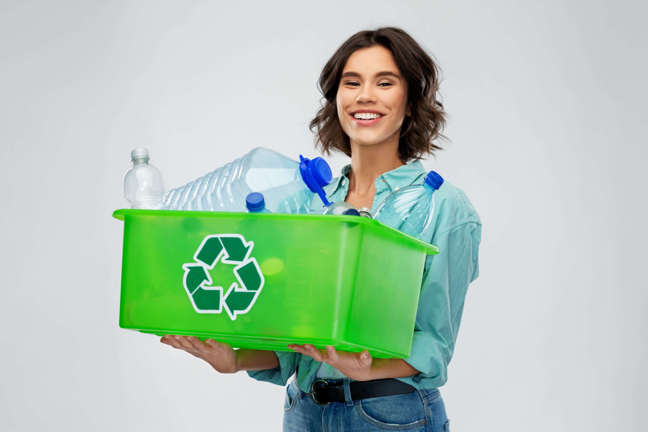 灰色の背景に緑色のリサイクル箱を持ち、環境に優しいライフスタイルのためにスペイン語で再利用可能および使い捨てのフレーズを学ぶ女性。 灰色の背景に緑色のリサイクル箱を持ち、環境に優しいライフスタイルのためにスペイン語で再利用可能および使い捨てのフレーズを学ぶ女性。