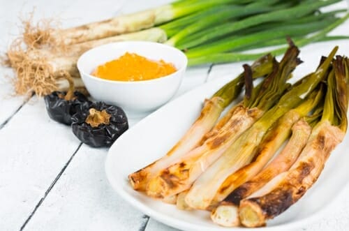 スペイン料理をイメージした、白い皿にネギと玉ねぎをグリルしたもの。