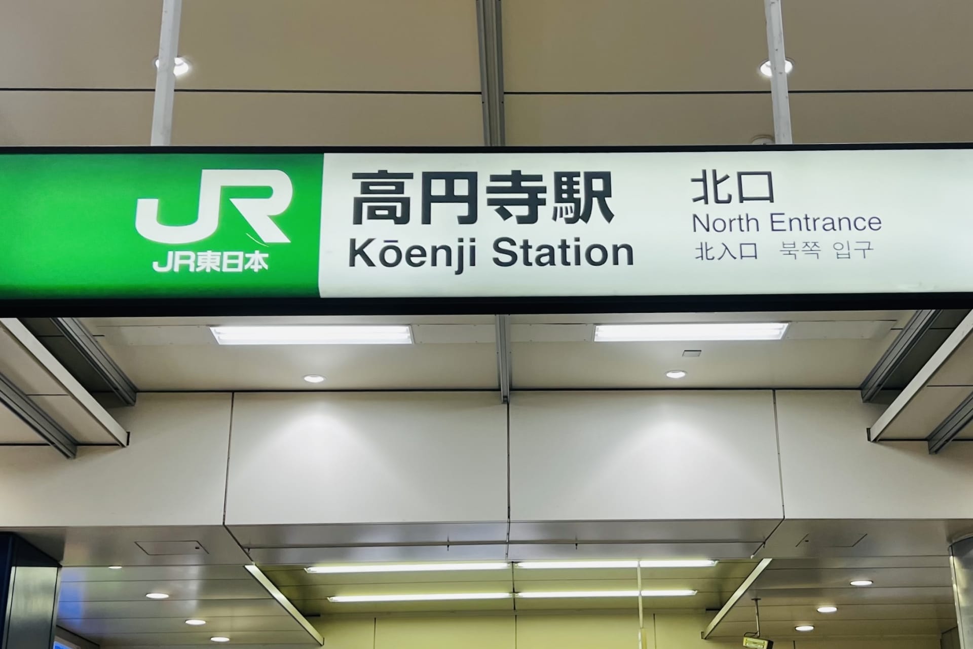 高円寺駅北口の標識。日本語、英語、韓国語の文字が書かれており、高円寺の活気ある多文化シーンを表現しています。.