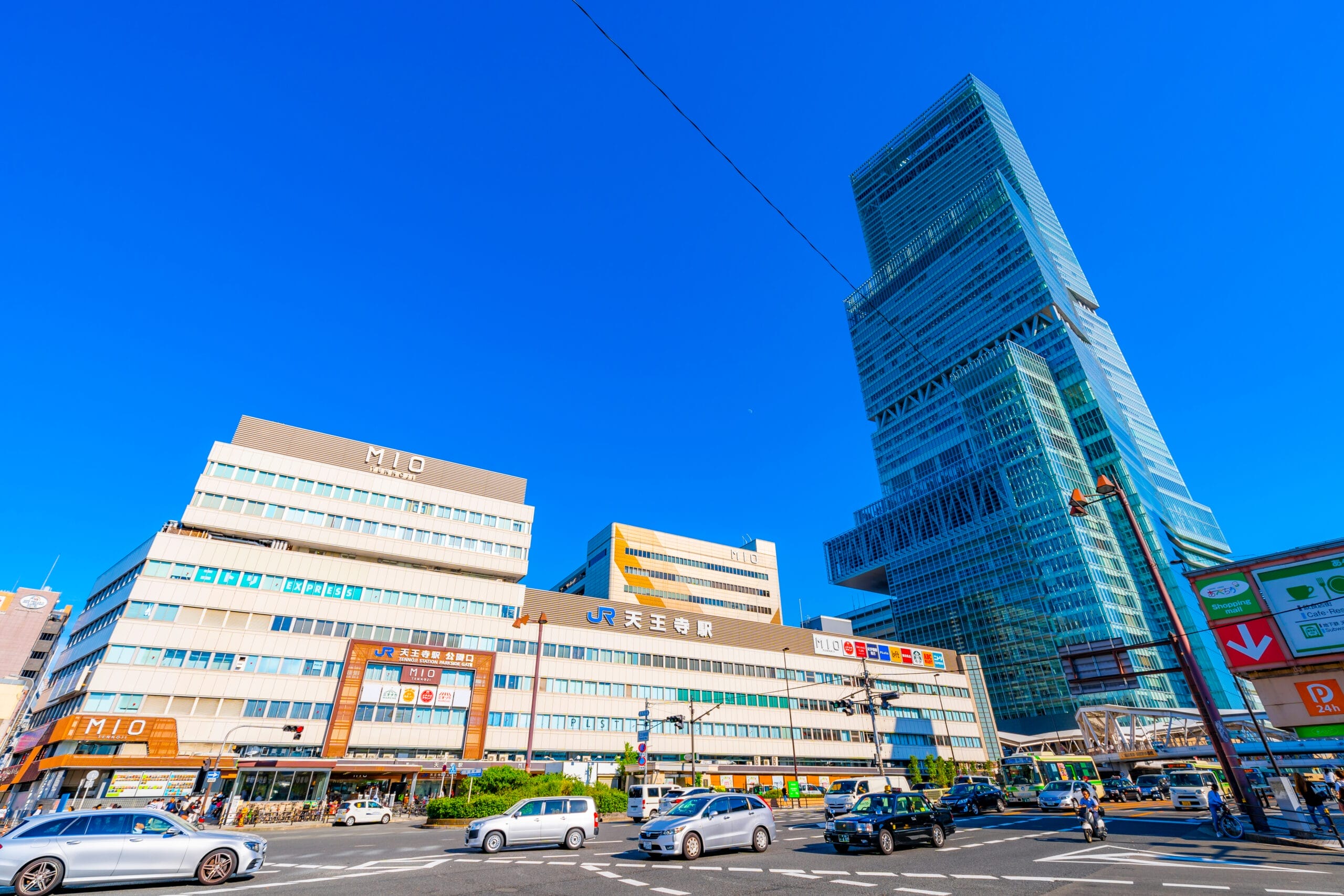賑やかな街並みの中に、小さな商業ビルの上にモダンな高層ビルがそびえ立ち、その下の通りを車が行き交い、澄み切った青空の下です。近くの天王寺では、地元の人々が文化交流と活気に満ちた都市生活を融合させた没入型のスペイン語教室マンツーマンセッションを楽しんでいます。.