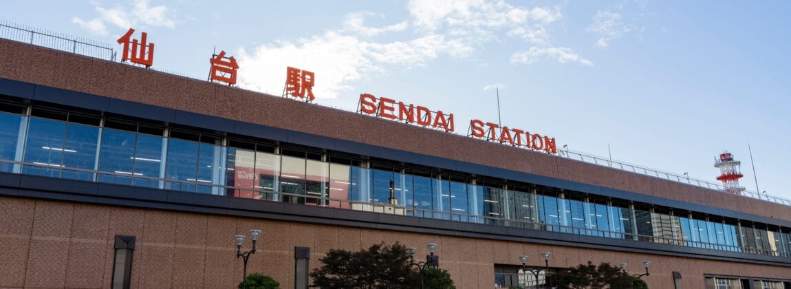 澄み切った青空と手前の木々を背景にした、宮城・仙台らしさをとらえた仙台駅の外観。.