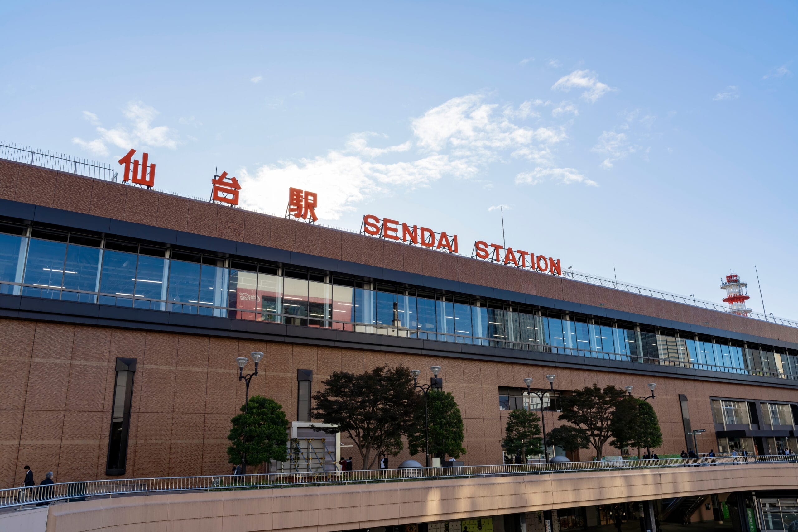 澄み切った青空と手前の木々を背景にした、宮城・仙台らしさをとらえた仙台駅の外観。.