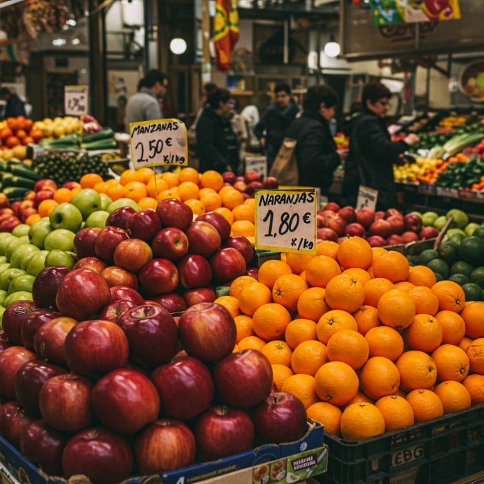 スペインの市場で野菜の値札（スペイン語表記）を見る客